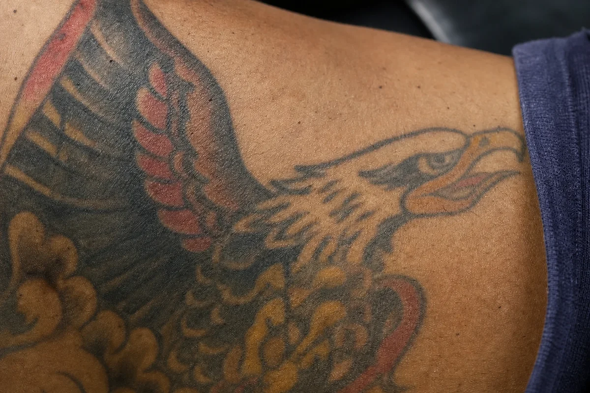Large colour traditional eagle tattoo in red, yellow and black across a chest and shoulder before laser removal