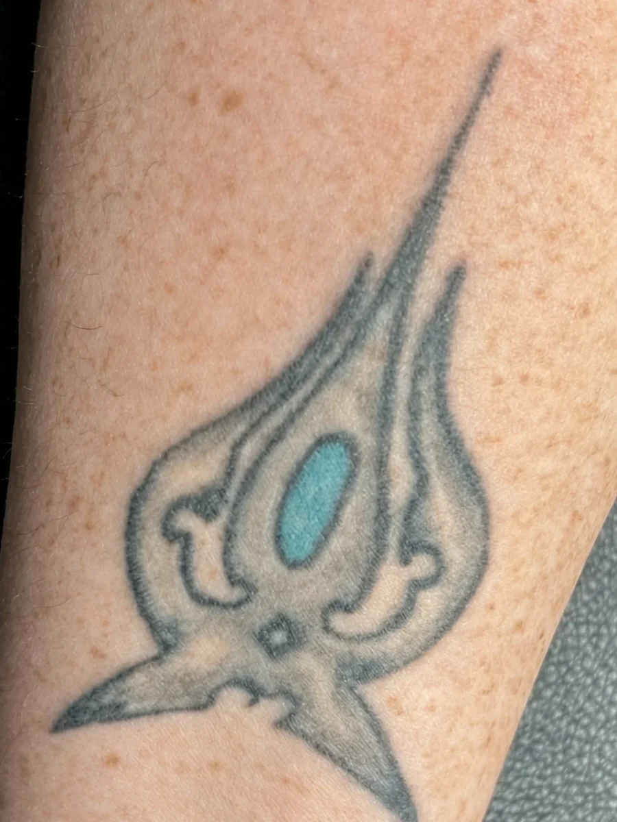 Black tribal tattoo with a teal centre on a forearm before laser tattoo removal