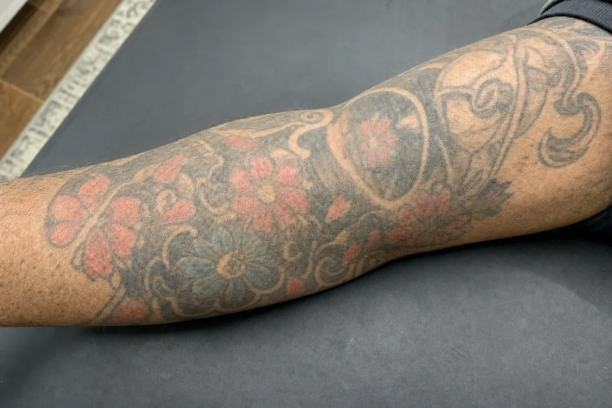 Colour Japanese-style floral sleeve tattoo with reds and blues on an arm before laser removal